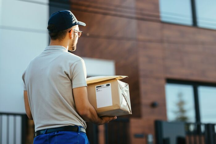 Man in a cap holding a package outside a modern building, showing people in boring industries behind the scenes.