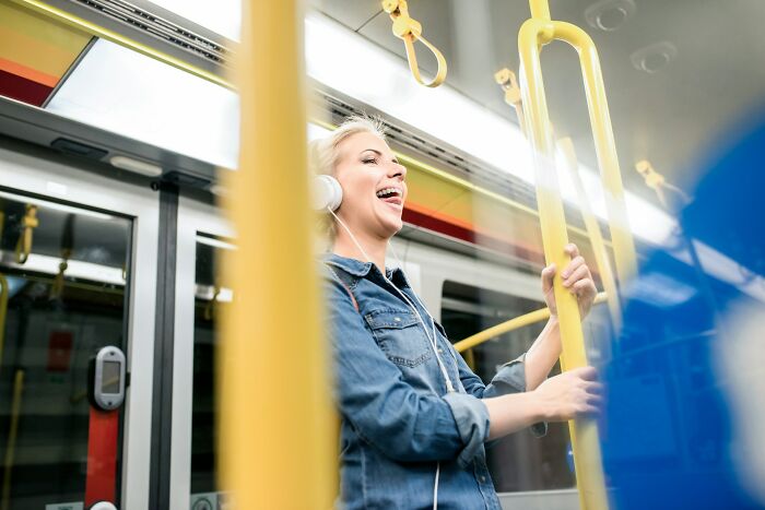 Young woman enjoying music on headphones while standing on a European tram, showcasing travel practices US may find weird