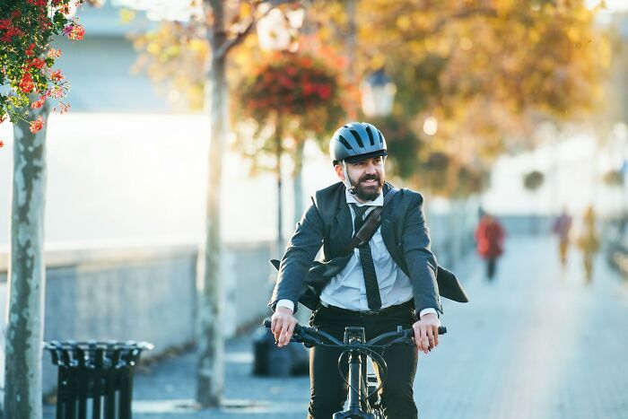 Man in business attire wearing a helmet riding a bike outdoors, highlighting daily dangers you might not realize.