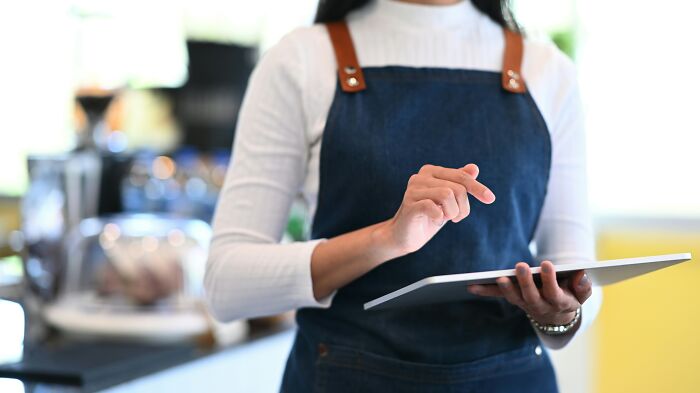 Person in an apron using a tablet indoors, representing stories about the worst coworkers making work a nightmare.