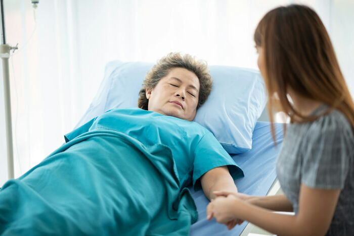 Hospital workers scene: elderly patient lying in bed holding a visitor's hand beside an IV pole in a bright room