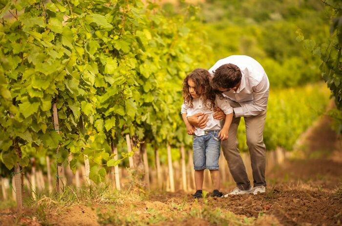 Man showing child around vineyard, illustrating rich people far from reality in a lush outdoor setting.