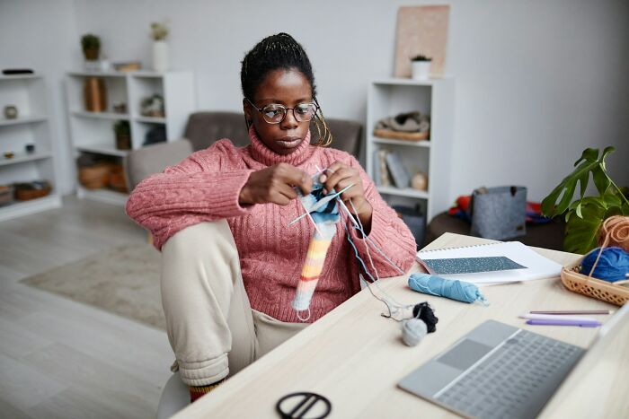 Woman knitting at home in a cozy sweater, practicing safety and comfort habits while living alone.