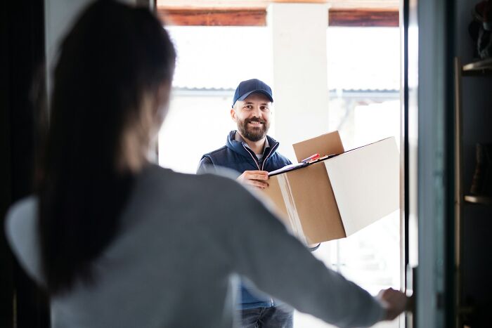 Delivery person holding a package at the door while a woman living alone opens the door for a safe interaction.