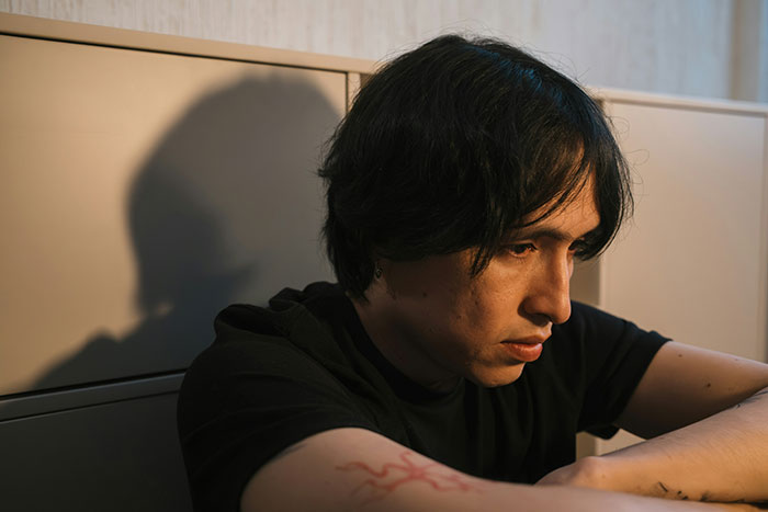 Young man suspecting cheating, sitting alone with a thoughtful expression, contemplating roommate and girlfriend secrets.