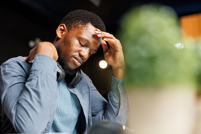 Young gifted man with headphones looks thoughtful and stressed while sitting indoors with blurred plant in foreground