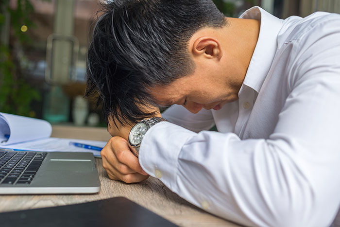 Tired gifted kid with potential resting head on arms at desk with laptop, showing frustration or exhaustion.