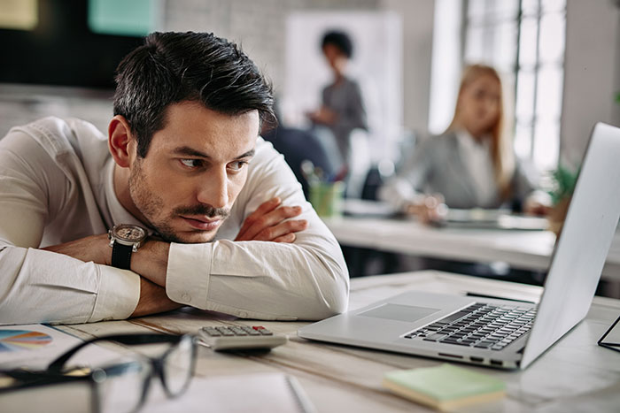 Young gifted man looking thoughtfully at laptop in an office, reflecting on potential to do great things.