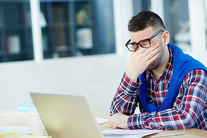 Man wearing glasses and a plaid shirt looking stressed while working on a laptop, representing gifted kids potential not realized.