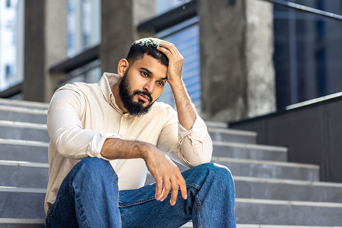 A young man sitting on outdoor steps, looking thoughtful and reflective about gifted kids and potential achievements.