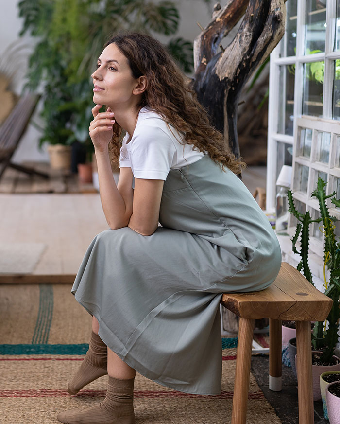 Thoughtful woman sitting indoors surrounded by plants, reflecting on gifted kids who had potential to do great things.