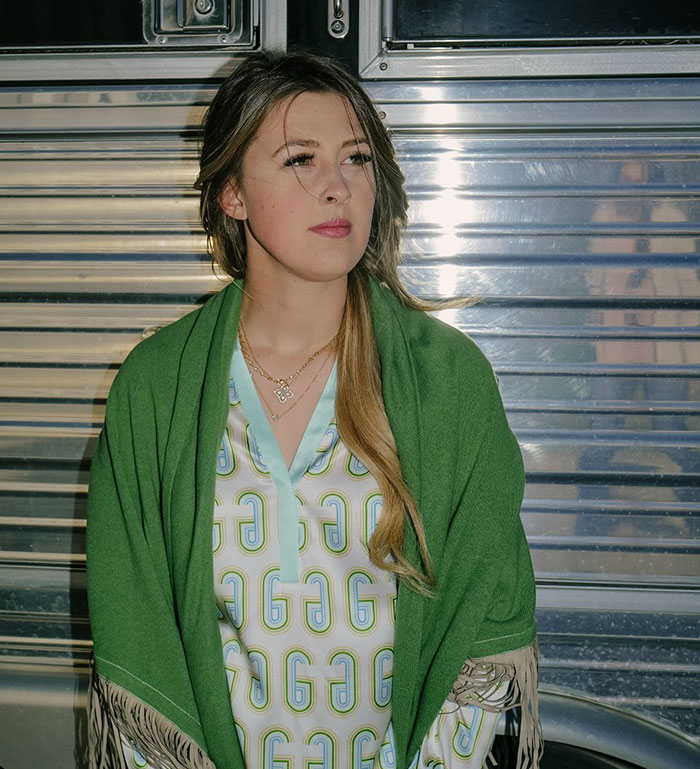 Young woman in a green shawl standing thoughtfully against a metallic background with Michael Schumacher health update theme.