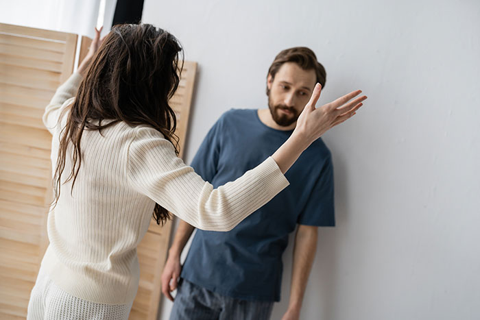 Woman arguing with boyfriend who looks emasculated as she gestures while fixing things in their home.