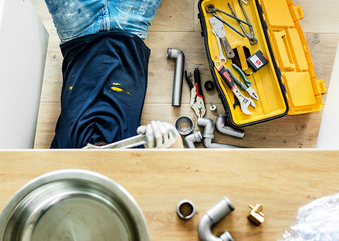 Man fixing plumbing pipes on the floor with tools and a toolbox, illustrating feelings of emasculation in relationships.