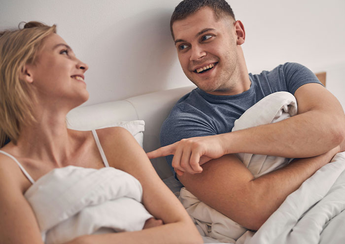 Couple in bed having a playful conversation, highlighting woman demanding swimmer boyfriend look like her friend&rsquo;s partner.
