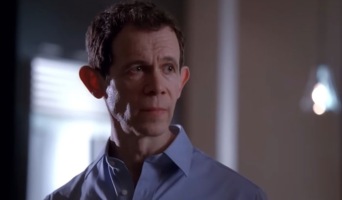 Man in blue shirt looking serious indoors, related to woman demands swimmer boyfriend story discussion.