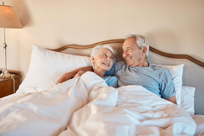 Elderly couple in a suite bedroom smiling and relaxing together during a visit, highlighting family and accommodation issues.