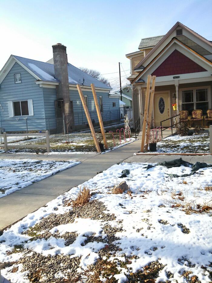 Poorly constructed wooden gate leaning awkwardly on a snowy sidewalk showing a major DIY fail outdoors.