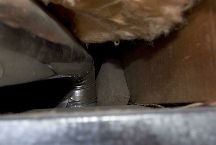 Close-up of a poorly installed HVAC duct with metal and insulation in a tight, unfinished space showing a DIY fail.