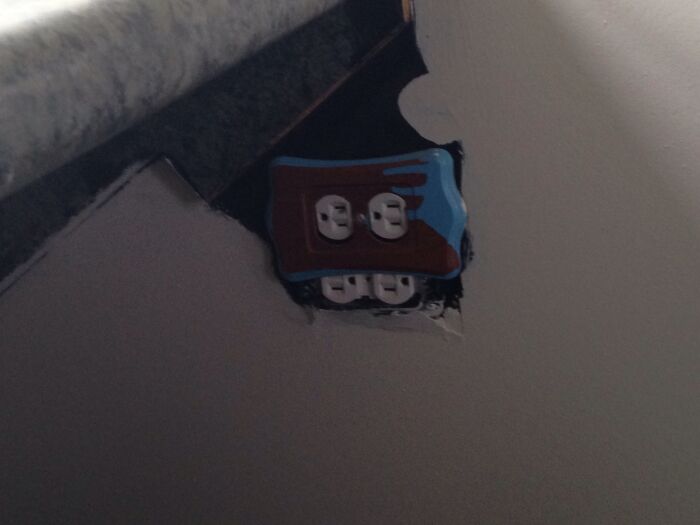 Poorly executed DIY electrical outlet installation on a wall with damaged drywall surrounding the outlet.