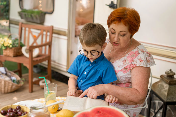 Grandma reading a book with her grandson at a table, illustrating family relationships and stepparent challenges.
