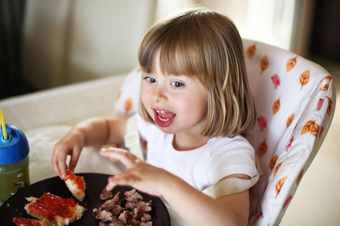 Young child eating food at a table, illustrating the relationship between grandma and her stepson in a family setting.