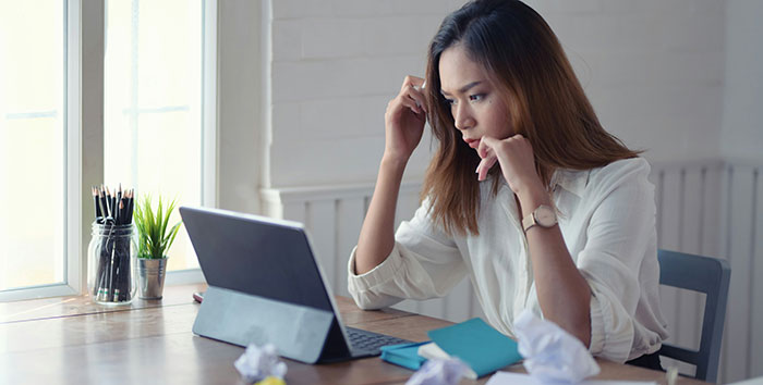 Woman using AI as her personal relationship coach on tablet, looking concerned while sitting at a desk with crumpled papers.