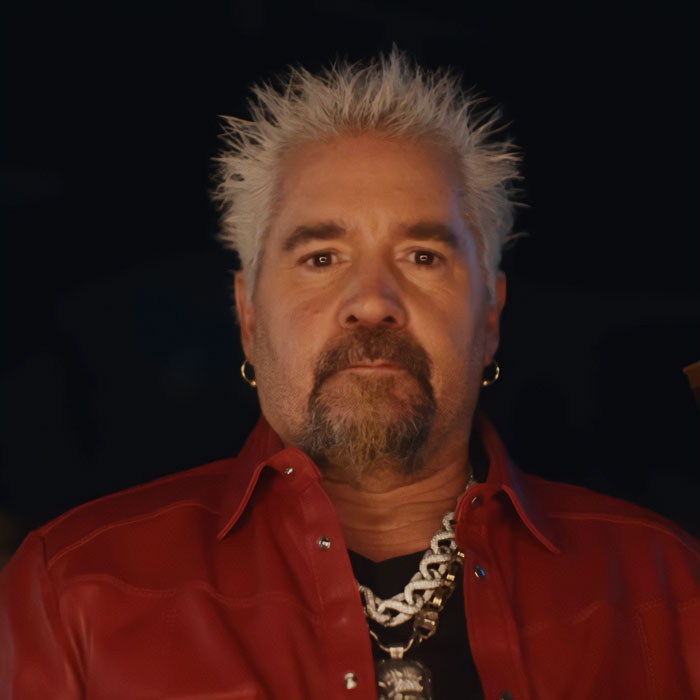 Guy Fieri in a red jacket with spiky blonde hair, showcasing his 58th birthday glow-up and new look.