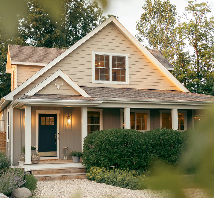 Cozy suburban American house with front porch and greenery, symbolizing pressing housing issues plaguing America at the moment.