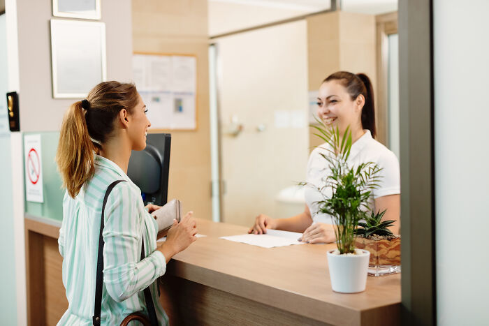 Two women smiling and talking at a reception desk, illustrating weird or shocking things people did in public without shame.