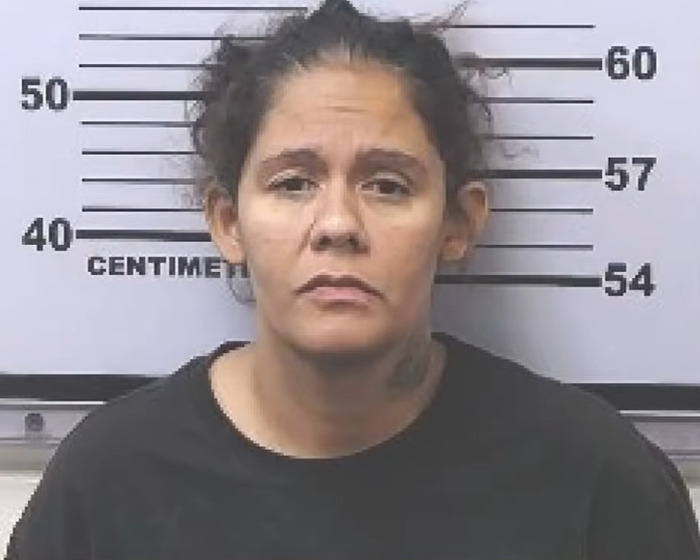 Mugshot of a woman with disheveled hair standing against a height chart related to girl abandoned in mobile home case.