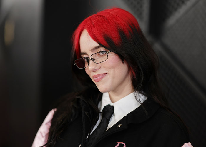 Young woman with red and black hair wearing glasses and a black jacket, representing hidden stories in famous songs insight.