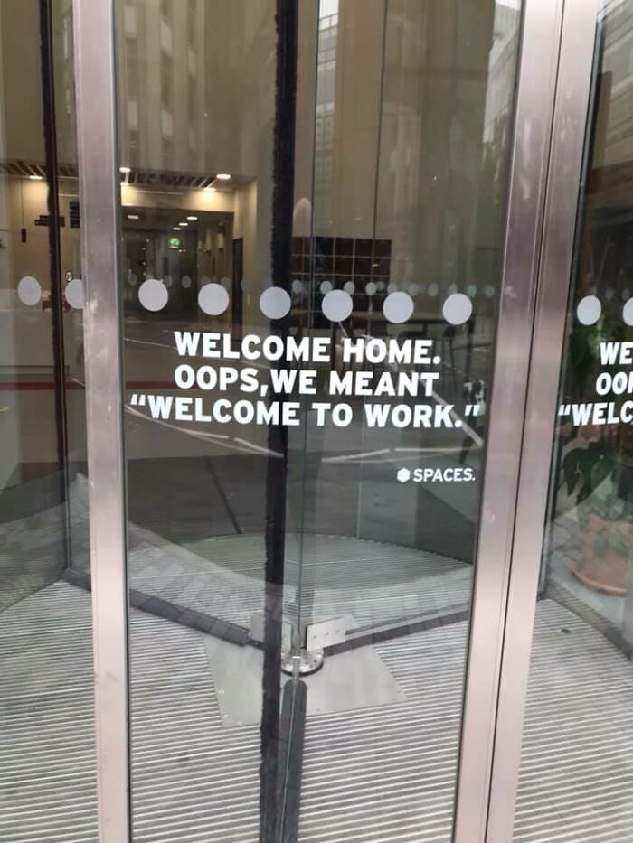 Glass revolving door with text referencing dystopia, welcoming workers ironically to work instead of home.