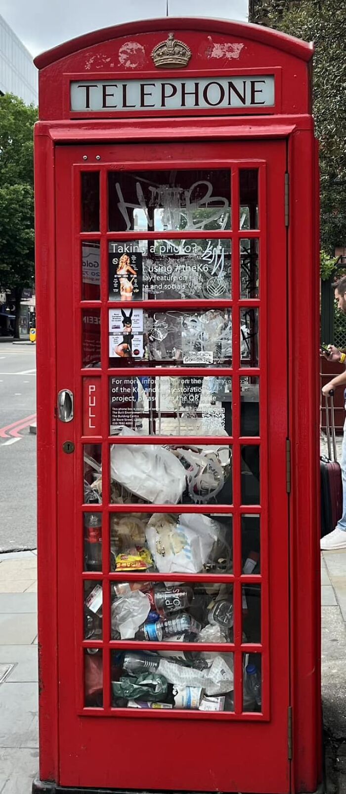 Red telephone booth filled with trash, illustrating signs of living in an actual dystopia in an urban street setting.