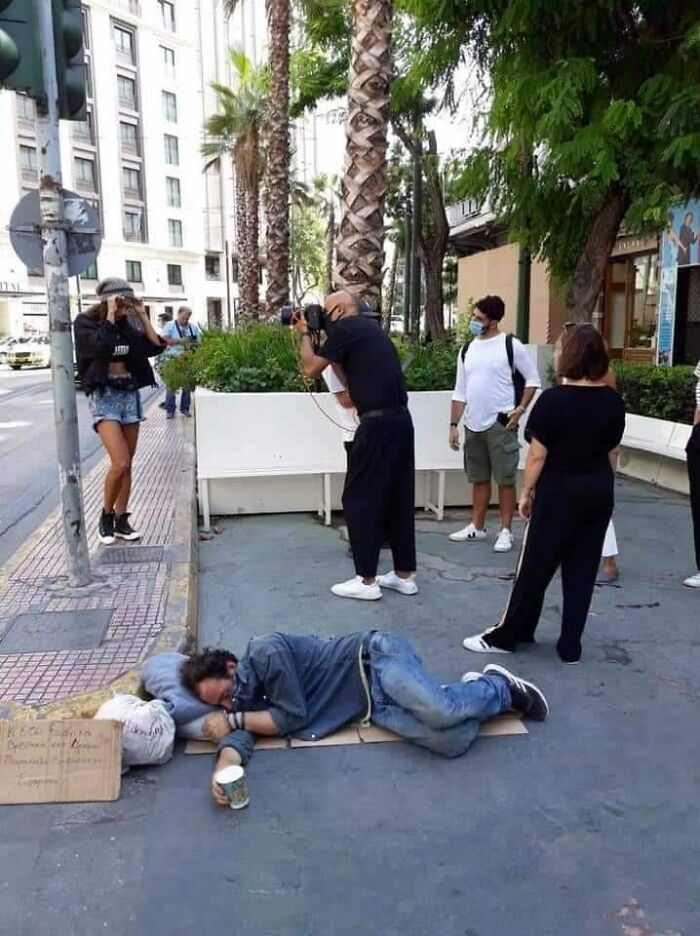 Photographer captures a woman posing near a homeless man lying on the sidewalk, illustrating modern dystopia realities.