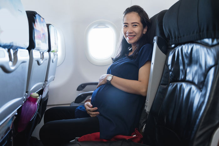 Pregnant woman smiling on an airplane seat, concerned about co-parenting with her bipolar husband after their breakup. Pregnant woman smiling on an airplane seat, concerned about co-parenting with her bipolar husband after their breakup.