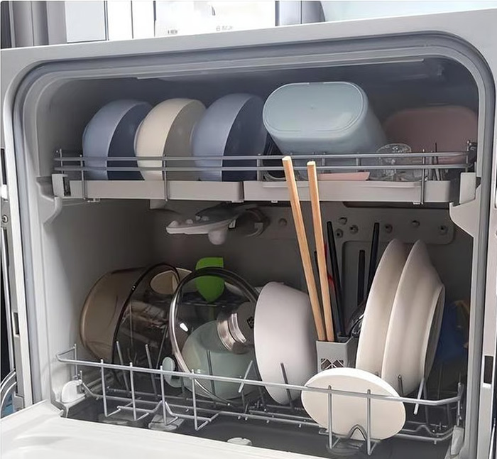 Open dishwasher loaded with clean dishes and kitchenware, highlighting a recently purchased household appliance.