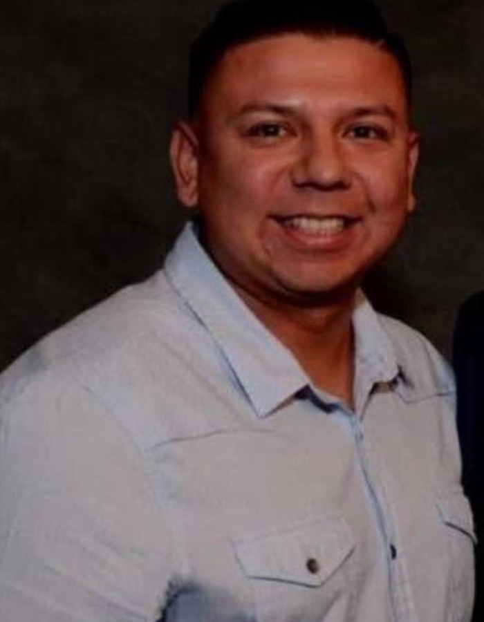 Smiling man in a light blue shirt against a dark background, related to teacher&rsquo;s life ends after diary affair discovery.