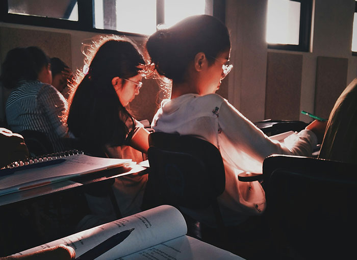 Student in classroom confidently sharing a fun fact with teacher while others focus on their work.