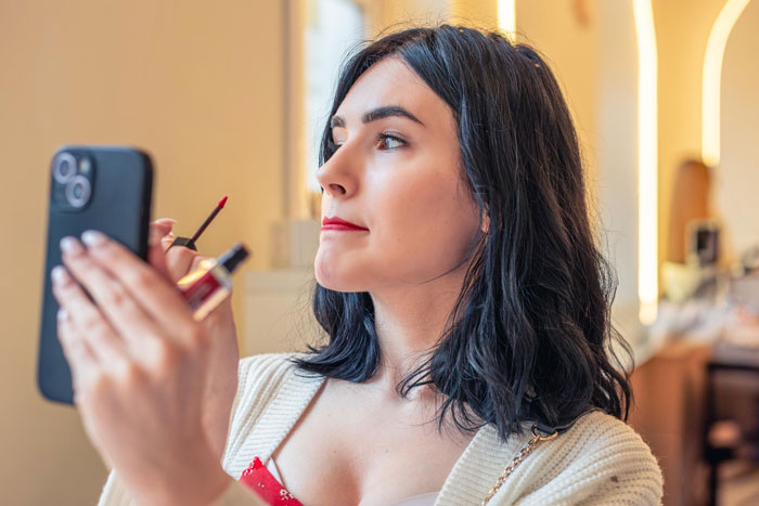 Young woman confidently applying lipstick while looking in her phone mirror, expressing her autonomy despite toxic behavior. Young woman confidently applying lipstick while looking in her phone mirror, expressing her autonomy despite toxic behavior.