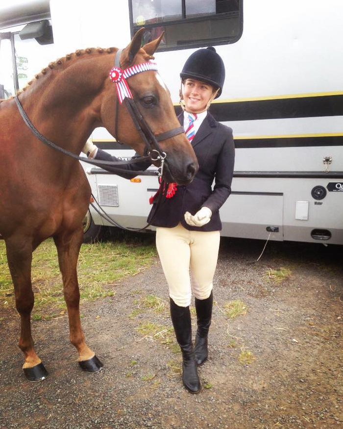 Woman in equestrian attire with awarded horse, reflecting on tragic loss and heartbreak after first anniversary.