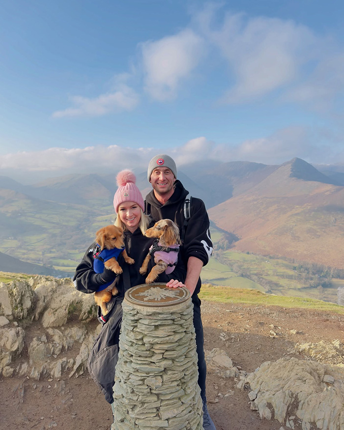 Husband and wife with two dogs on a mountain hike, capturing a moment before tragic loss on first anniversary.