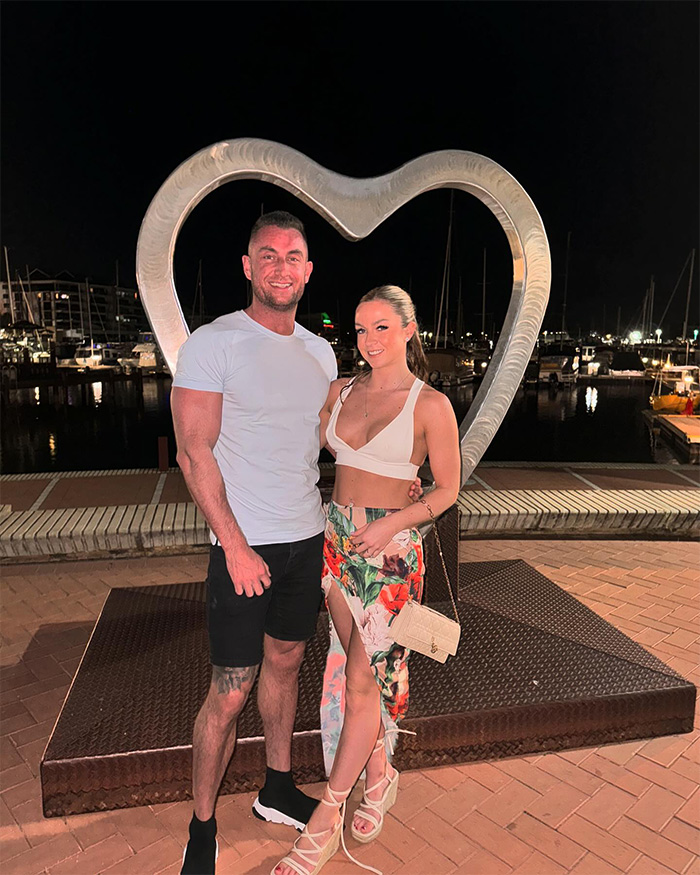 Couple posing together at night near heart-shaped sculpture by marina, representing husband heartbroken after wife&rsquo;s tragic loss.