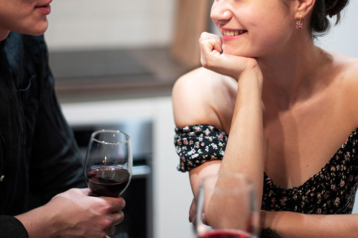 Woman trusting husband and smiling while sharing a conversation over glasses of red wine in a cozy setting