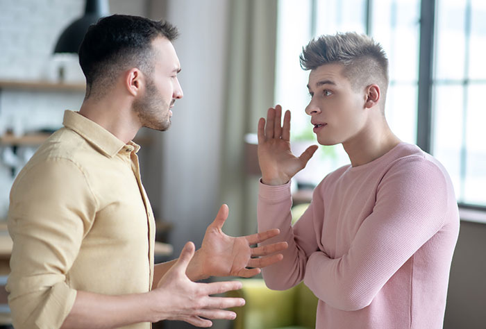 Two men in a heated discussion indoors, depicting a man torn between his husband and mother-in-law after helping her secretly.