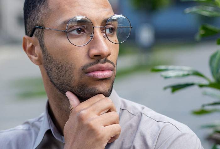 Man with glasses looking thoughtful and torn between his husband and mother-in-law while outdoors.