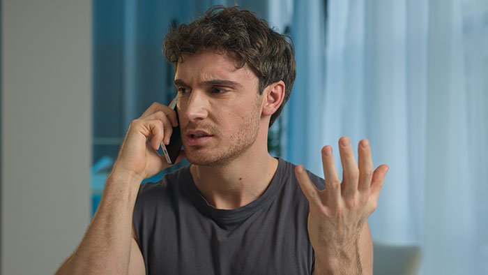 Frustrated husband on phone gesturing, depicting husband cancer diagnosis excuses and tense conversation at home.