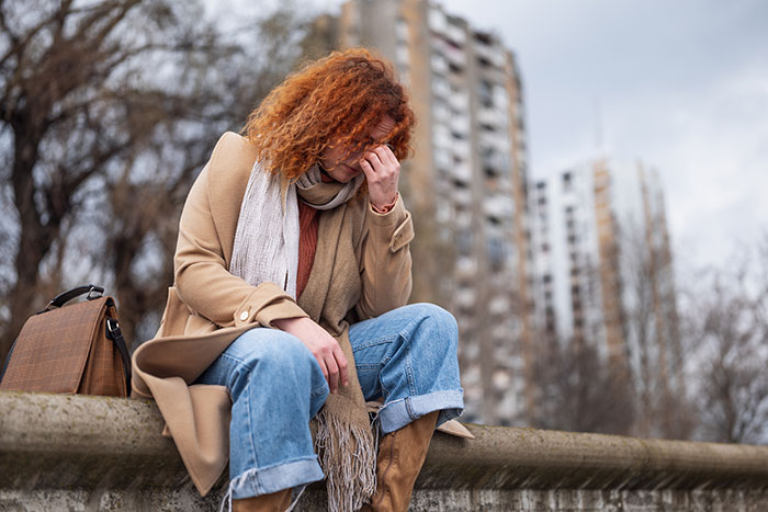 Upset woman sitting on ledge in city, holding face, concept of husband cancer diagnosis excuses and emotional distress.