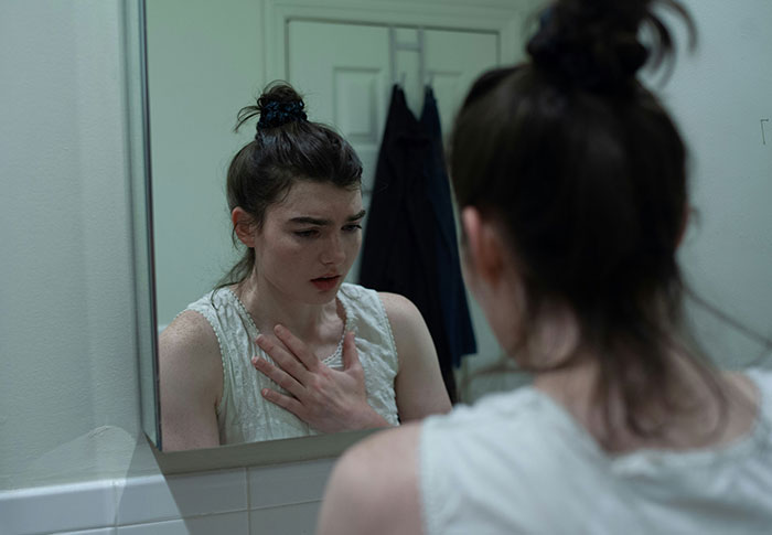 Young woman looking upset and frustrated in a bathroom mirror, reflecting feelings of being skinny-shamed and body positivity conflict.