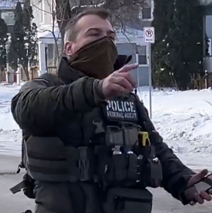 Minneapolis ICE agent wearing tactical gear and face covering gestures while speaking outdoors in snowy neighborhood. Minneapolis ICE agent wearing tactical gear and face covering gestures while speaking outdoors in snowy neighborhood.